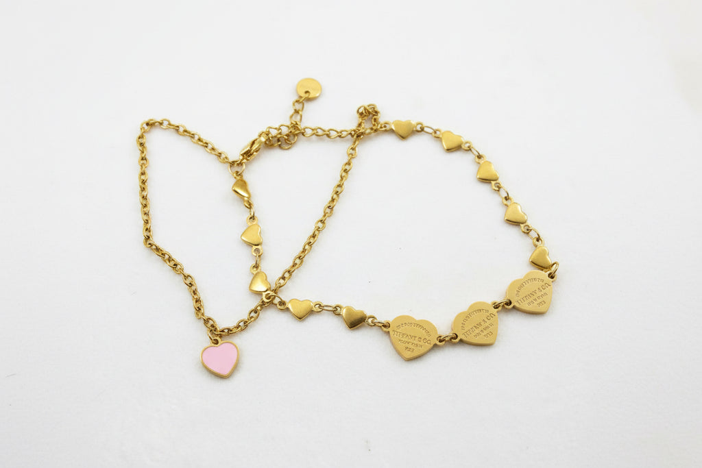 Gold double bracelet with a pink heart charm and gold heart charms.