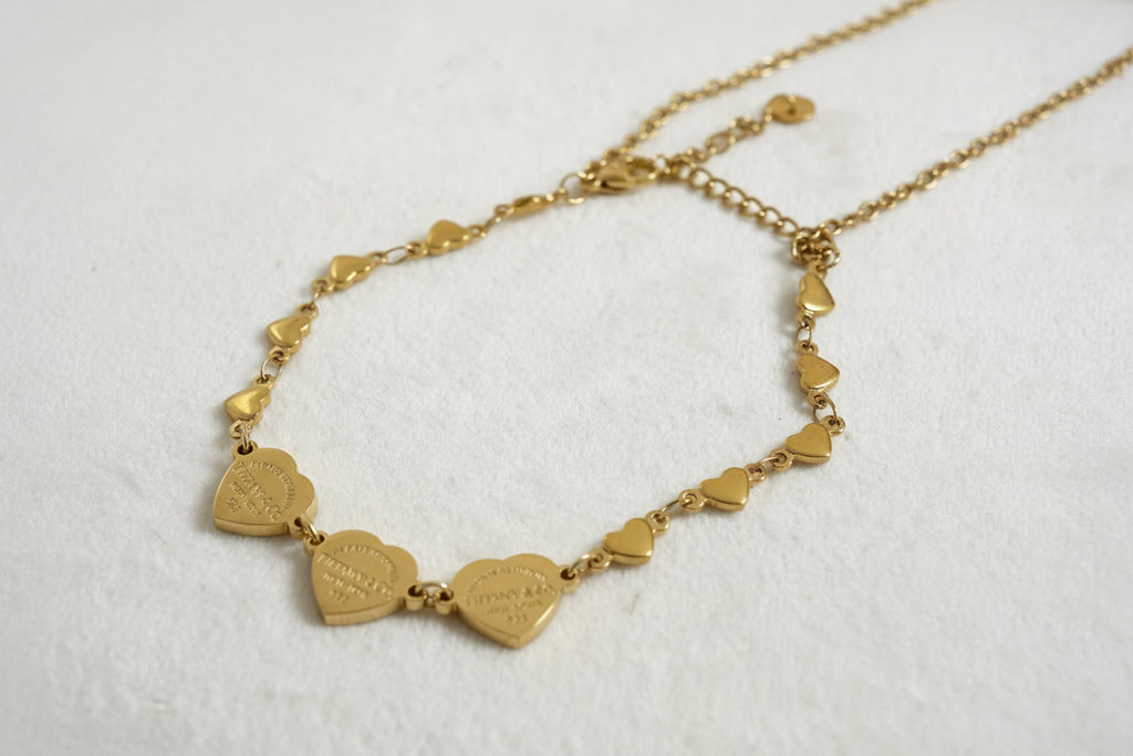 Gold double bracelet with a pink heart charm and gold heart charms.