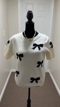 White sweater with black bow patterns on a mannequin against a white wall.