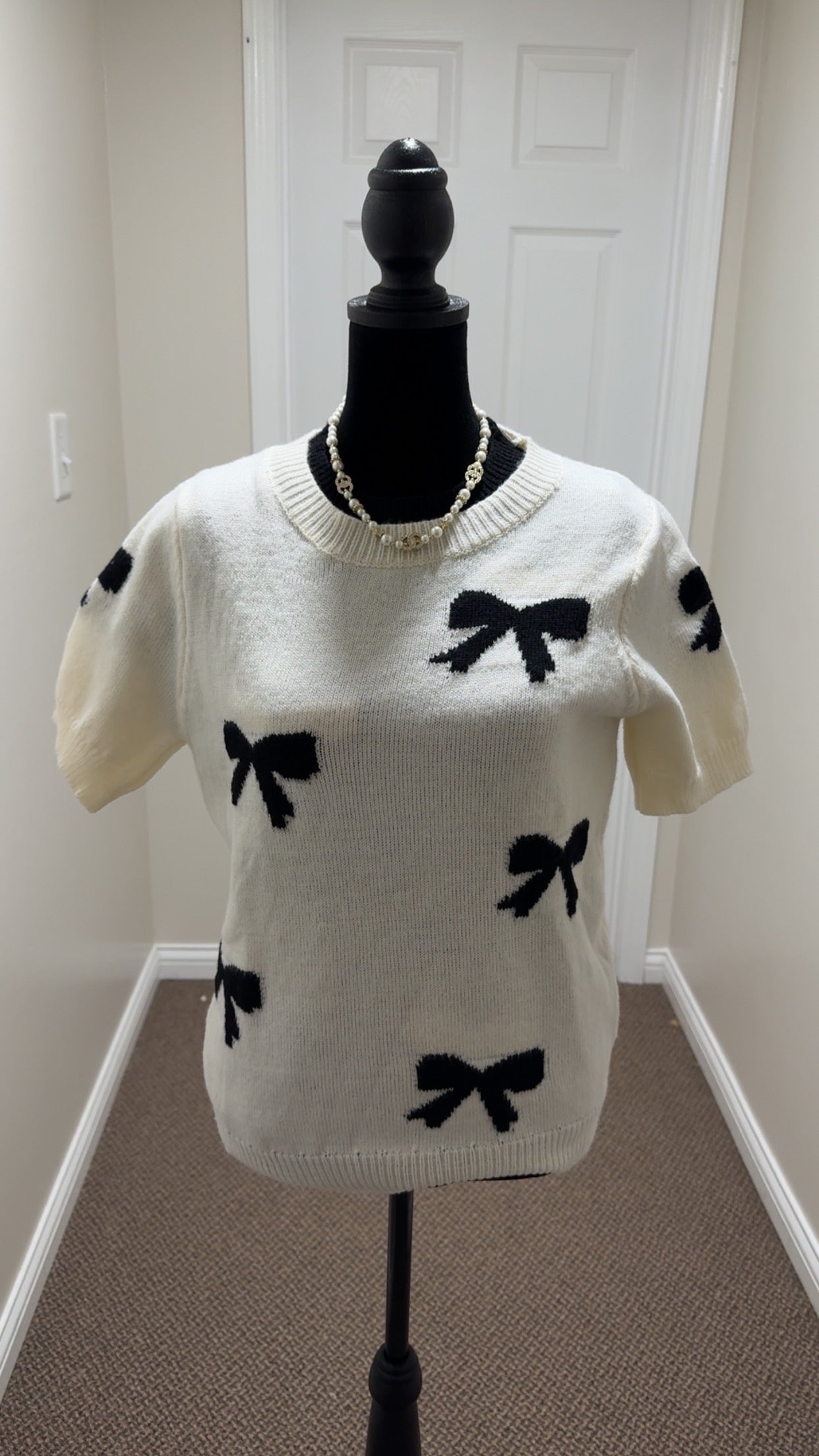 White sweater with black bow patterns on a mannequin against a white wall.