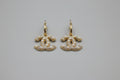 Gold earrings with pearl-like stones on a speckled ceramic dish.