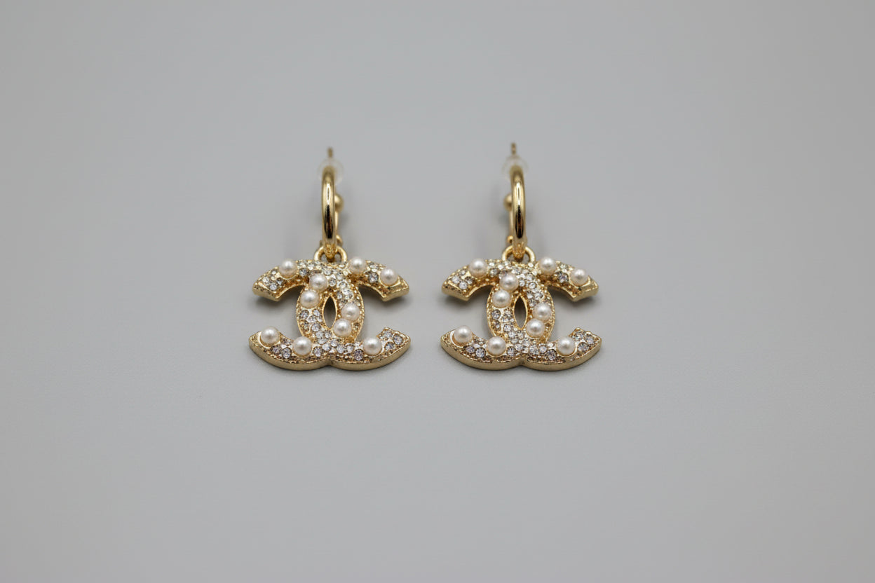 Gold earrings with pearl-like stones on a speckled ceramic dish.